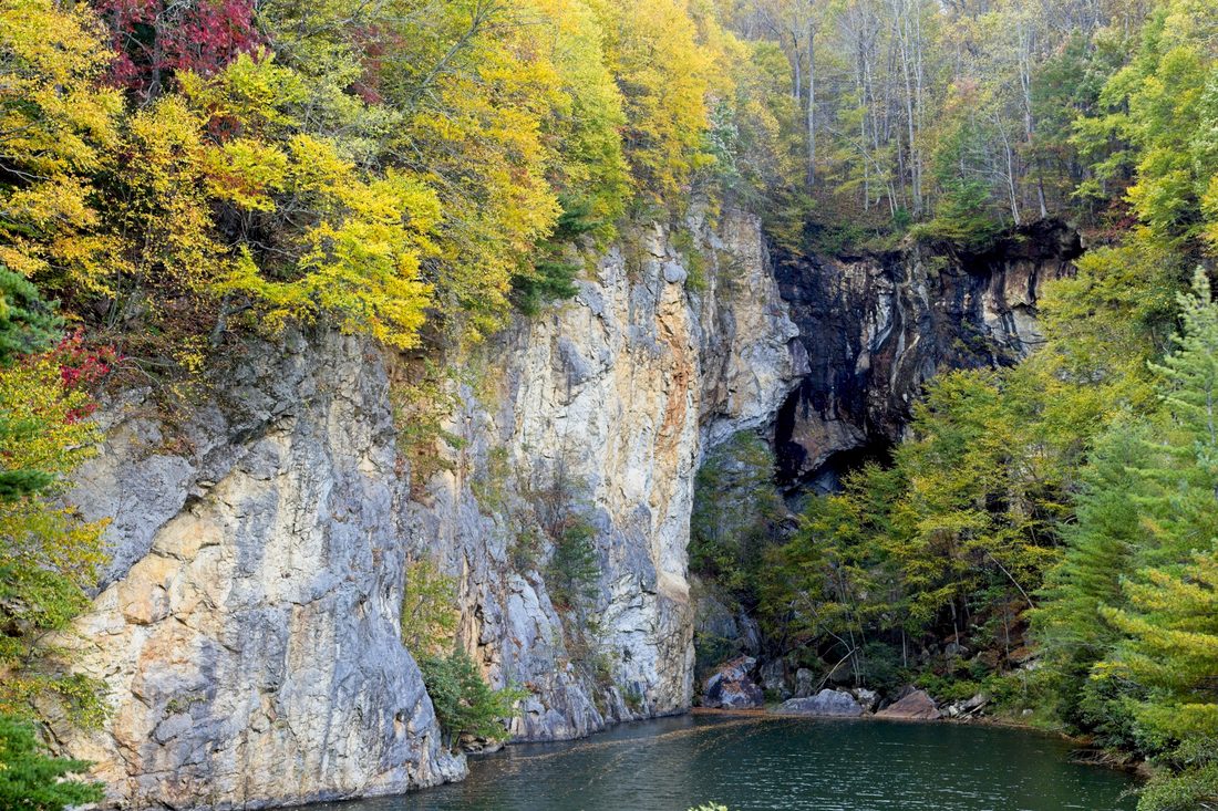 Pale rock cliff above a still pond ringed with red and gold autumn foliage