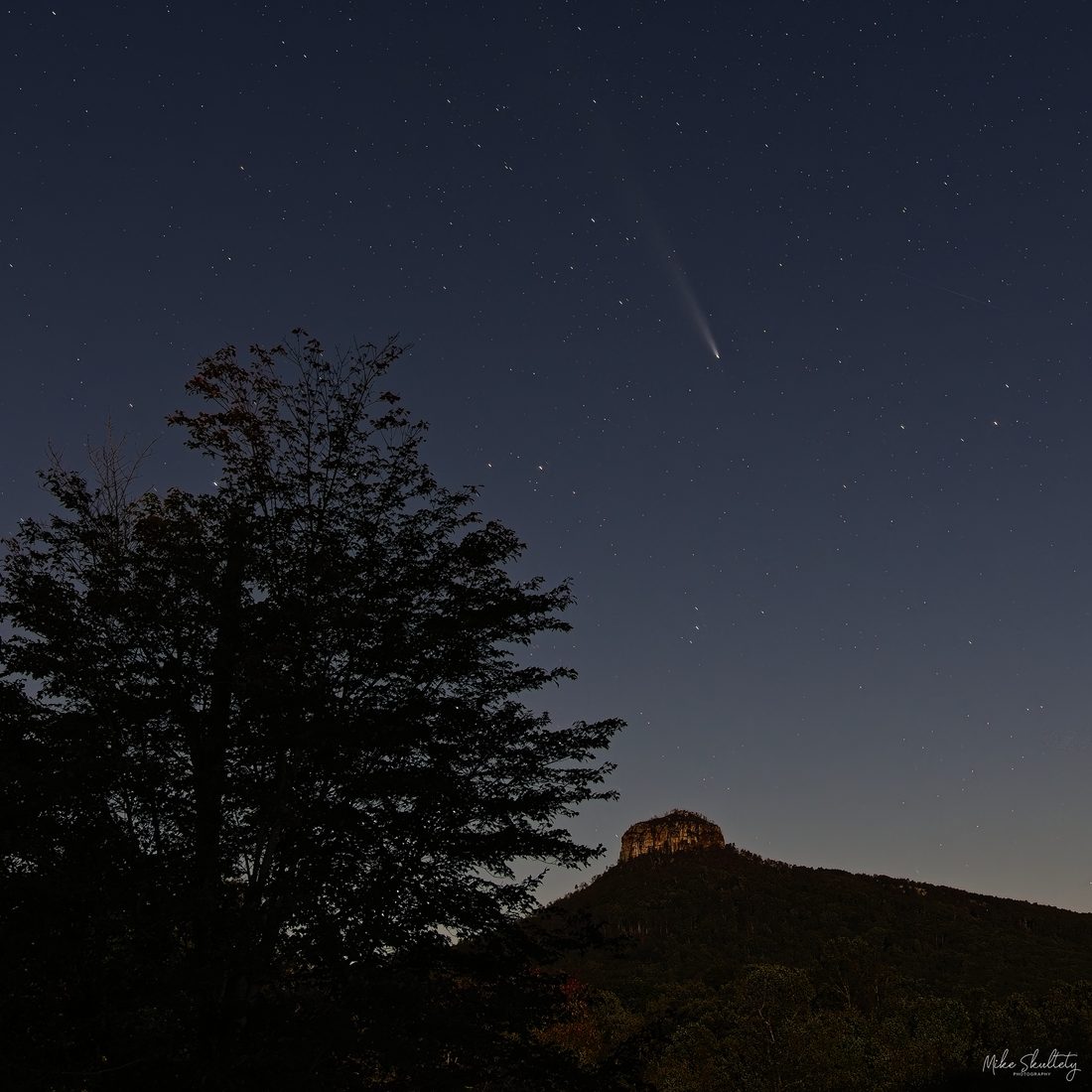 Comet streaking above Pilot Mountain silhouette under a starry twilight sky
