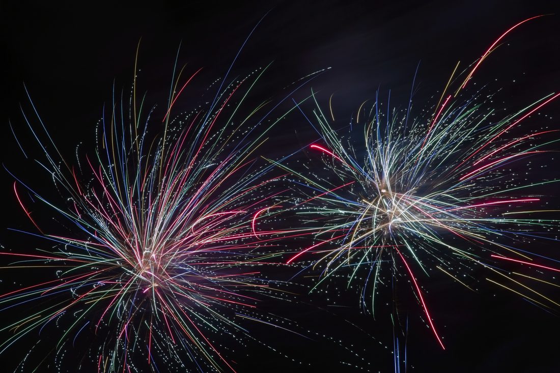 Multicolored fireworks exploding in chaotic rainbow filaments against black sky