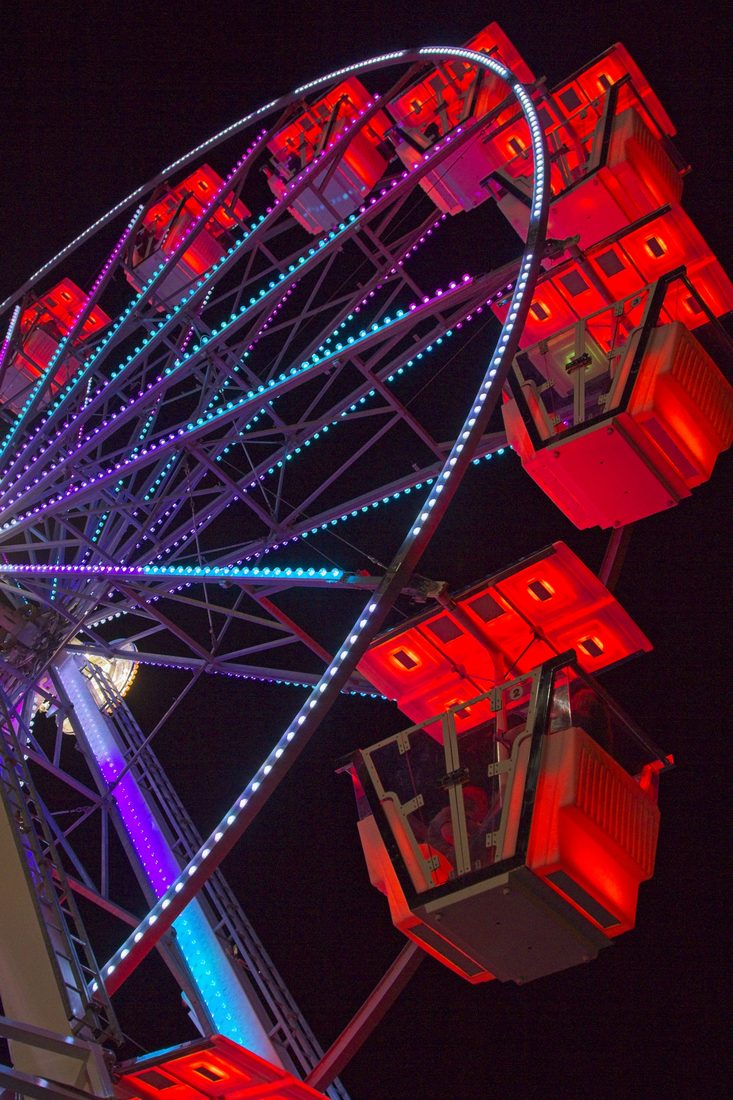 Illuminated ferris wheel cars glowing red and electric blue against the night