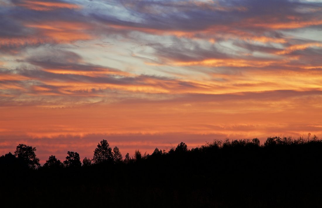 Patterned cloud bands stretching across a sunset sky above a hazy valley