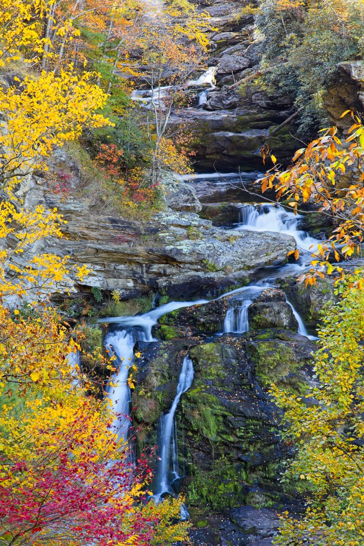 Tiered autumn cascade weaving down rock face through fiery yellow and red foliage